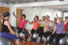 Gruppe von Frauen auf Gymnastikbällen, die an einer Fitnessstunde mit Übungsbändern teilnehmen.