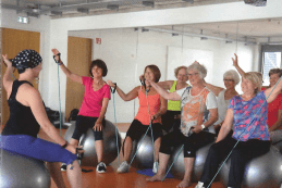Gruppe von Frauen auf Gymnastikbällen, die an einer Fitnessstunde mit Übungsbändern teilnehmen.