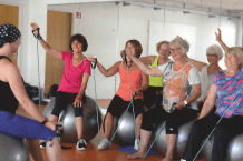 Gruppe von Frauen auf Gymnastikb&auml;llen, die an einer Fitnessstunde mit &Uuml;bungsb&auml;ndern teilnehmen.