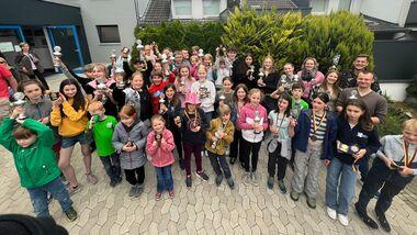 Gruppenzusammenstellung von Kindern und Jugendlichen mit Pokalen vor einem Gebäude und Bäumen im Hintergrund.