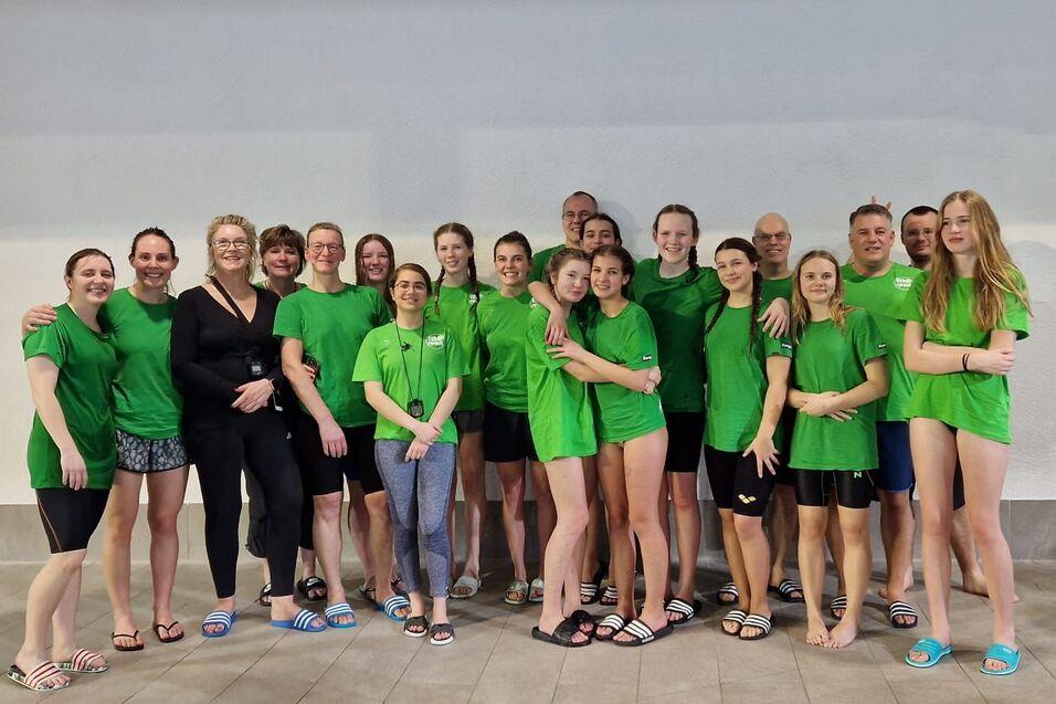 Gruppe von Schwimmern in gr&uuml;nen T-Shirts posiert zusammen in einem Schwimmbad, Hintergrunde hell und neutral.