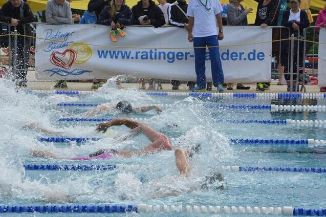 Schwimmer im Wettkampf spritzen Wasser auf einer wettkampforientierten Schwimmbahn, Zuschauer im Hintergrund.