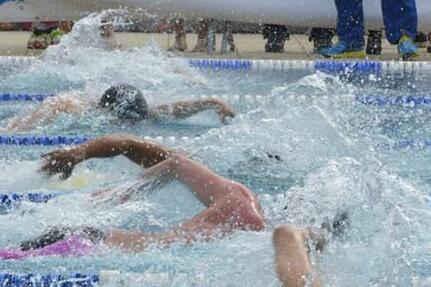 Schwimmer im Wettkampf spritzen Wasser auf einer wettkampforientierten Schwimmbahn, Zuschauer im Hintergrund.