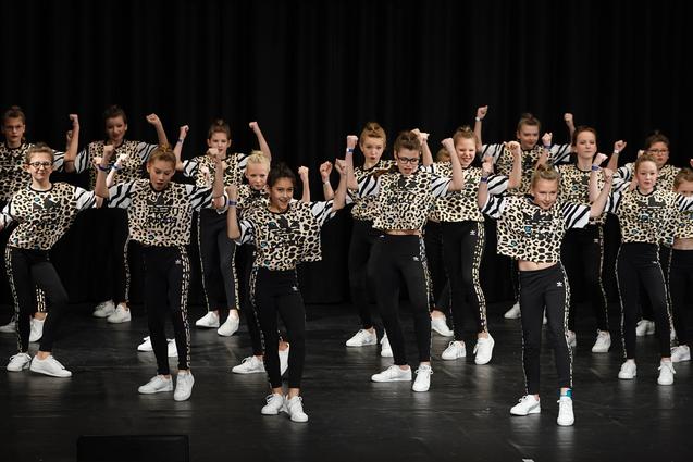 Gruppe von tanzenden M&auml;dchen in Leoparden-Outfits auf einer B&uuml;hne, schwarzer Hintergrund und schwaches Licht.