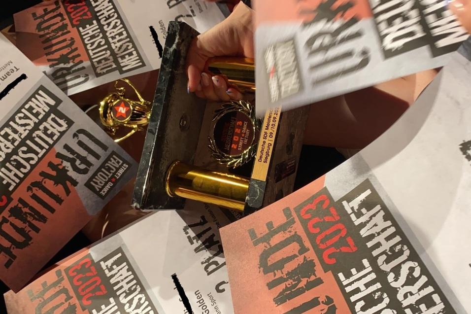 Trophäe und Urkunden für den zweiten Platz bei der Deutschen Meisterschaft 2023 in der Hand einer Person.