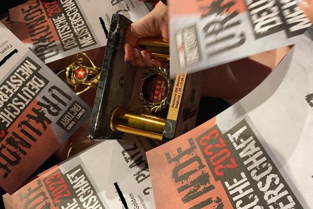 Trophäe und Urkunden für den zweiten Platz bei der Deutschen Meisterschaft 2023 in der Hand einer Person.