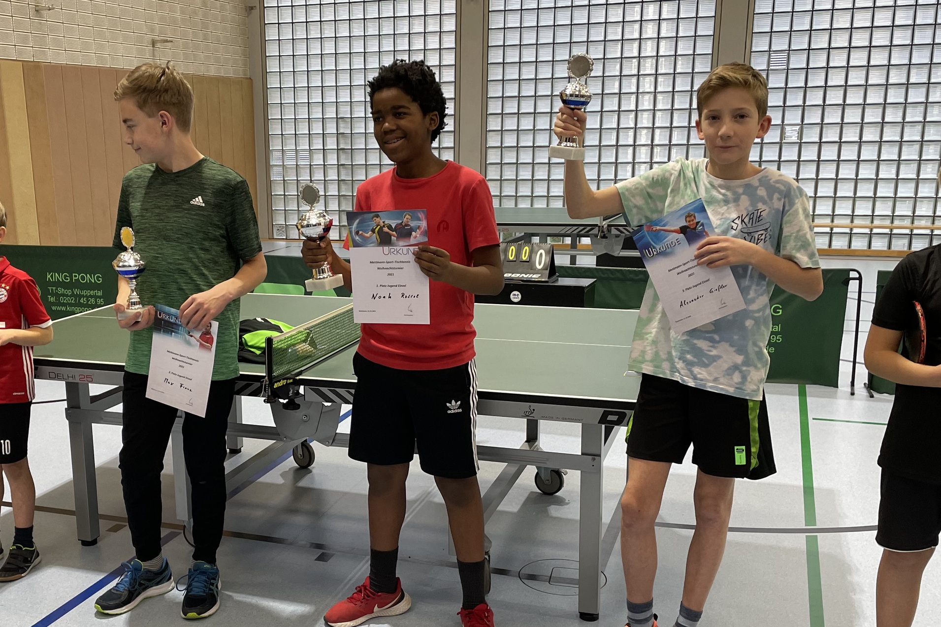 Vier Kinder stehen an einem Tischtennistisch, halten Pokale und Urkunden nach einem Wettbewerb.