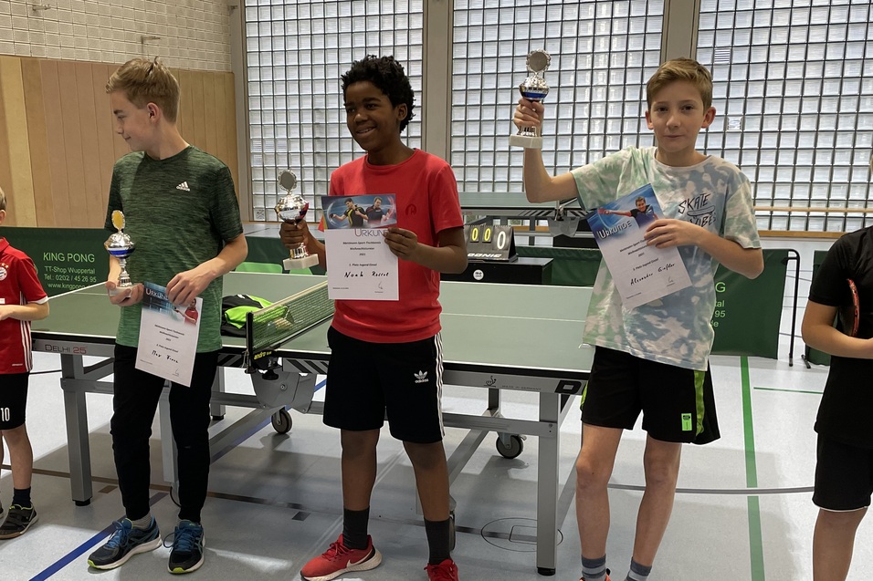Vier Kinder stehen an einem Tischtennistisch, halten Pokale und Urkunden nach einem Wettbewerb.