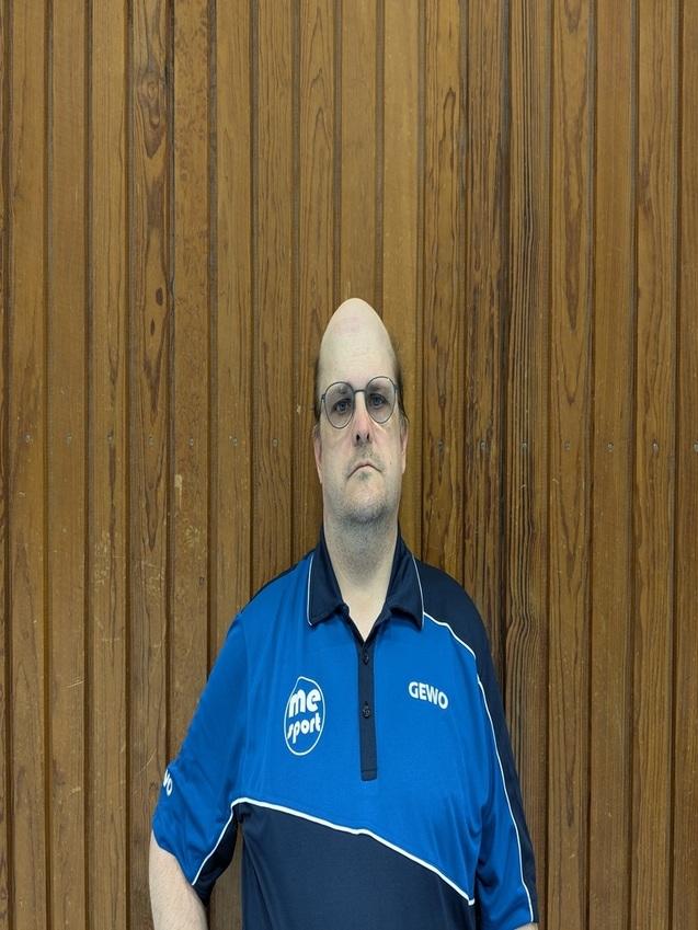 Porträt eines Mannes mit Glatze und Brille, der ein blaues Sportpoloshirt vor einer Holzwand trägt.