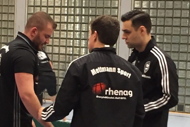 Drei M&auml;nner in Sportjacken stehen an einem Tischtennistisch und sprechen miteinander.