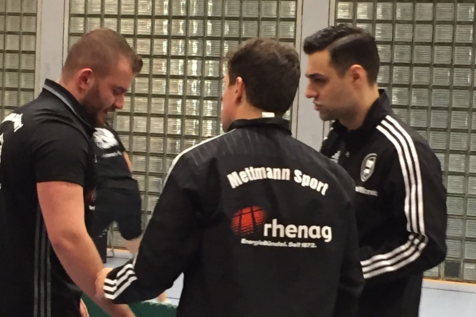 Drei Männer in Sportjacken stehen an einem Tischtennistisch und sprechen miteinander.