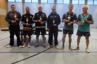 Sechs Tischtennisspieler stehen mit Pokalen in einer Sporthalle, umgeben von einer Tischtennisplatte.