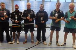 Sechs Tischtennisspieler stehen mit Pokalen in einer Sporthalle, umgeben von einer Tischtennisplatte.