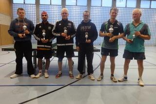 Sechs Tischtennisspieler stehen mit Pokalen in einer Sporthalle, umgeben von einer Tischtennisplatte.