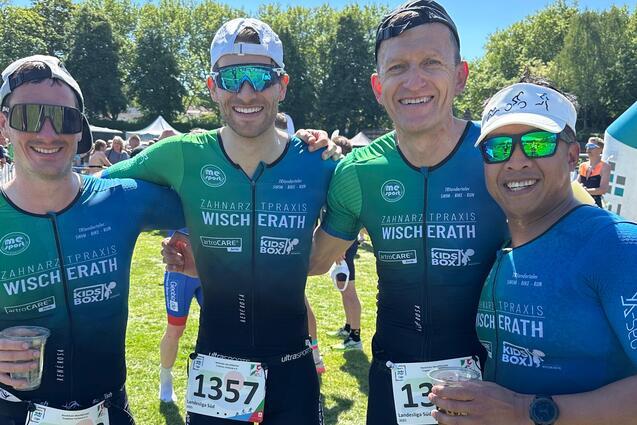 Vier Männer in Sporttrikots posieren lächelnd auf einer grünen Wiese nach einem Wettkampf.