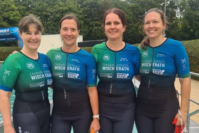 Vier Frauen in Neoprenanzügen stehen barfuß am Poolrand und lächeln in die Kamera. Grünes und blaues Triton-Logo sichtbar.