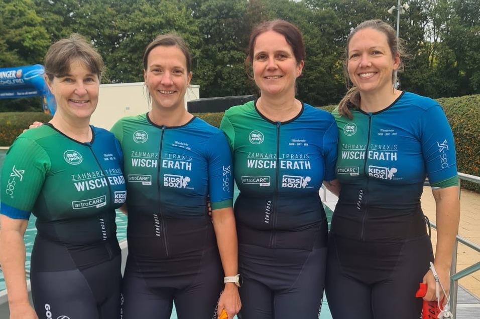 Vier Frauen in Neoprenanzügen stehen barfuß am Poolrand und lächeln in die Kamera. Grünes und blaues Triton-Logo sichtbar.