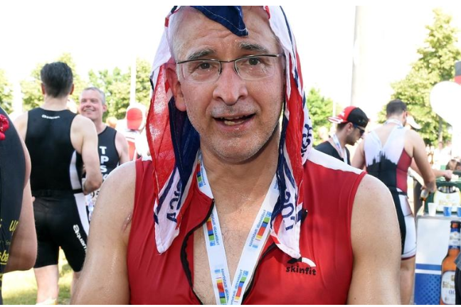 Ein erschöpfter Teilnehmer in Sportkleidung mit einer Medaille und Handtuch um den Kopf nach einem Triathlon-Event.