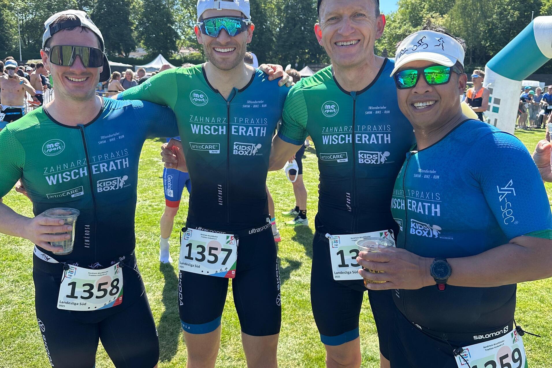 Vier Männer in Sporttrikots posieren lächelnd auf einer grünen Wiese nach einem Wettkampf.