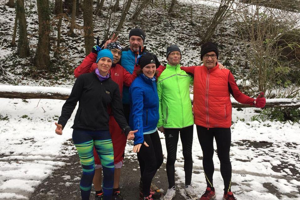 Sechs Personen posieren im Schnee; einige tragen Laufbekleidung und zeigen fröhliche Gesten.
