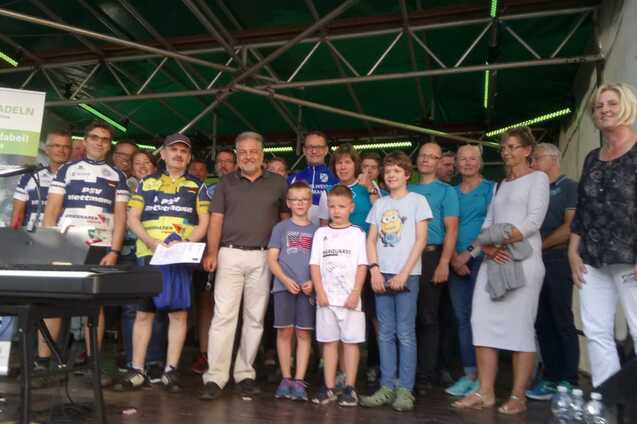 Gruppenevent mit Teilnehmenden in Sportbekleidung auf einer Bühne, daneben ein Klavier und ein Plakat der Stadt Radeln.