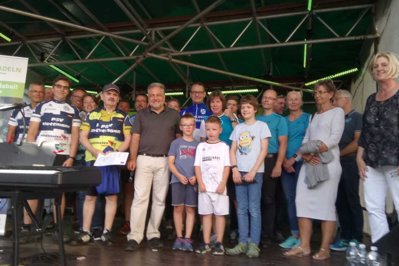 Gruppenevent mit Teilnehmenden in Sportbekleidung auf einer Bühne, daneben ein Klavier und ein Plakat der Stadt Radeln.