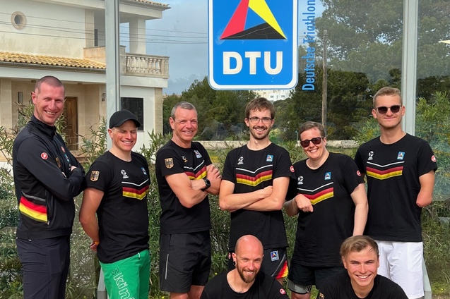 Eine Gruppe von acht Athleten in DTU-Trikots posiert vor dem DTU-Logo auf einem sonnigen Tag im Freien.