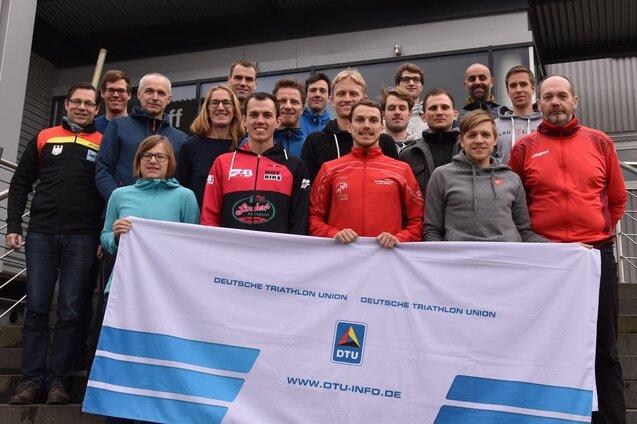 Gruppe von Triathleten posiert vor einem Gebäude, hält eine Flagge der Deutschen Triathlon Union.