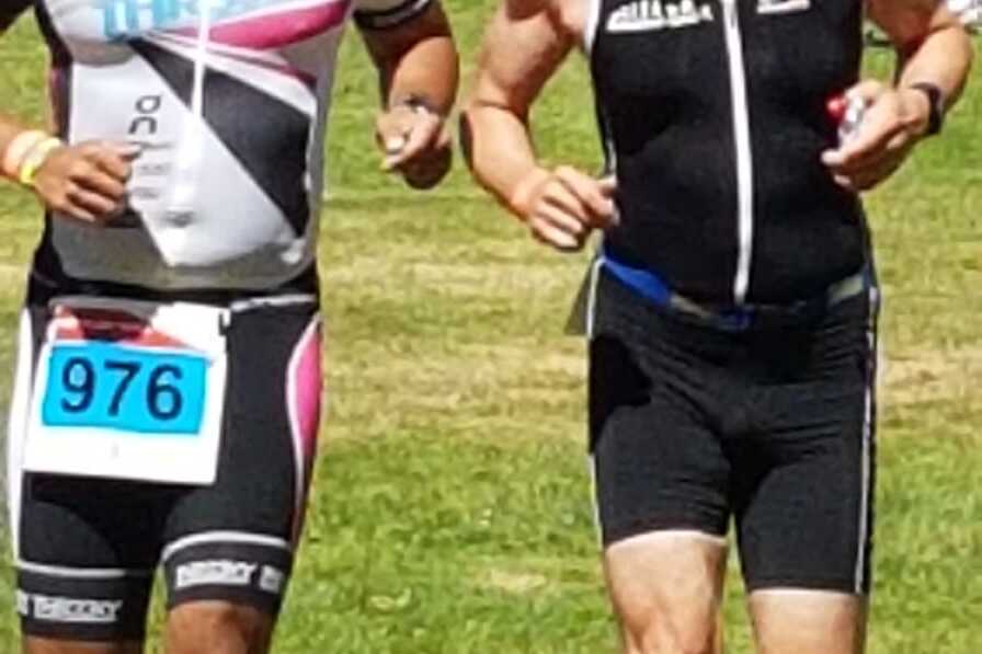 Zwei M&auml;nner in Sportkleidung laufen nebeneinander auf einer Rasenfl&auml;che bei einem Triathlon-Event.