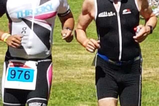 Zwei Männer in Sportkleidung laufen nebeneinander auf einer Rasenfläche bei einem Triathlon-Event.