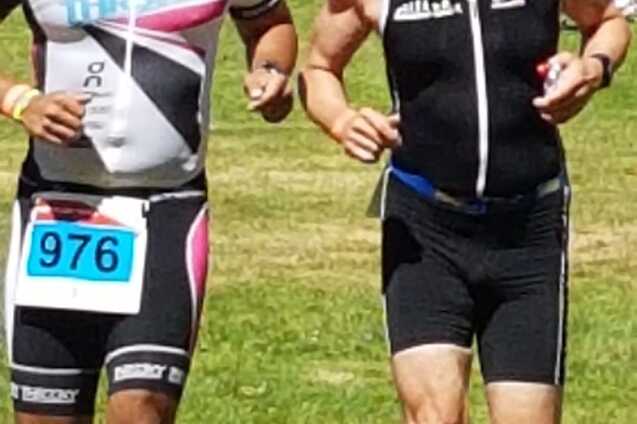 Zwei M&auml;nner in Sportkleidung laufen nebeneinander auf einer Rasenfl&auml;che bei einem Triathlon-Event.