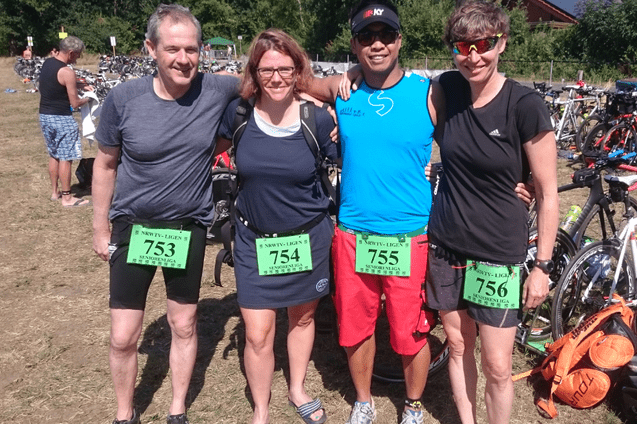 Vier sportliche Teilnehmer stehen gemeinsam auf einer Rasenfläche, umgeben von Fahrrädern, mit Wettkampfnummerschildern.