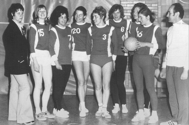Gruppe weiblicher Sportlerinnen in Trikots mit Nummern, posierend in einer Halle mit einem Basketball.