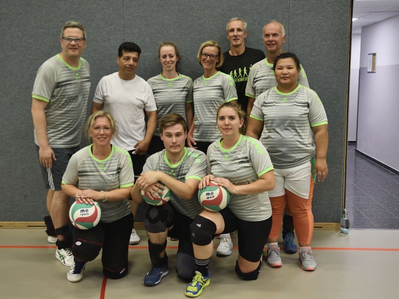 Gruppenfoto von zehn Personen in Sportkleidung, posierend mit Volleyballen in einer Sporthalle.
