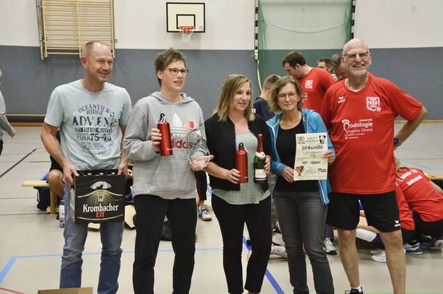 Fünf Personen stehen in einer Sporthalle und halten Trophäen sowie Urkunden nach einem Wettkampf in den Händen.