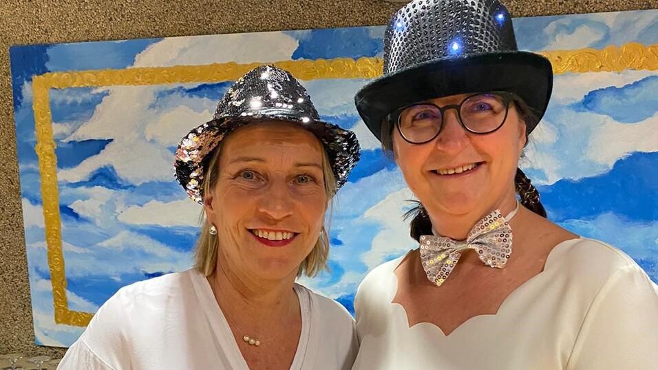 Auf dem Bild sind zwei weibliche Personen zu sehen. Links steht steffi und rechts Vera. Beide haben ein weißes Oberteil und einen Schwarz/ Silbernen Paillettenhut an.