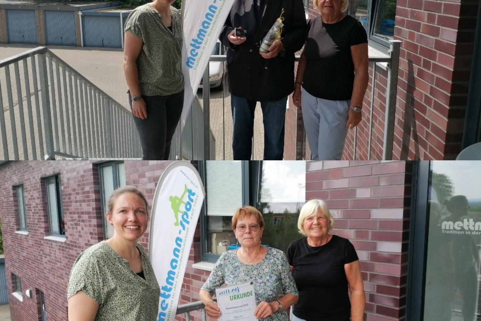 Zwei Gruppen von Personen posieren vor einem Gebäude mit einem Fahnenmast und einer Auszeichnung in den Händen.
