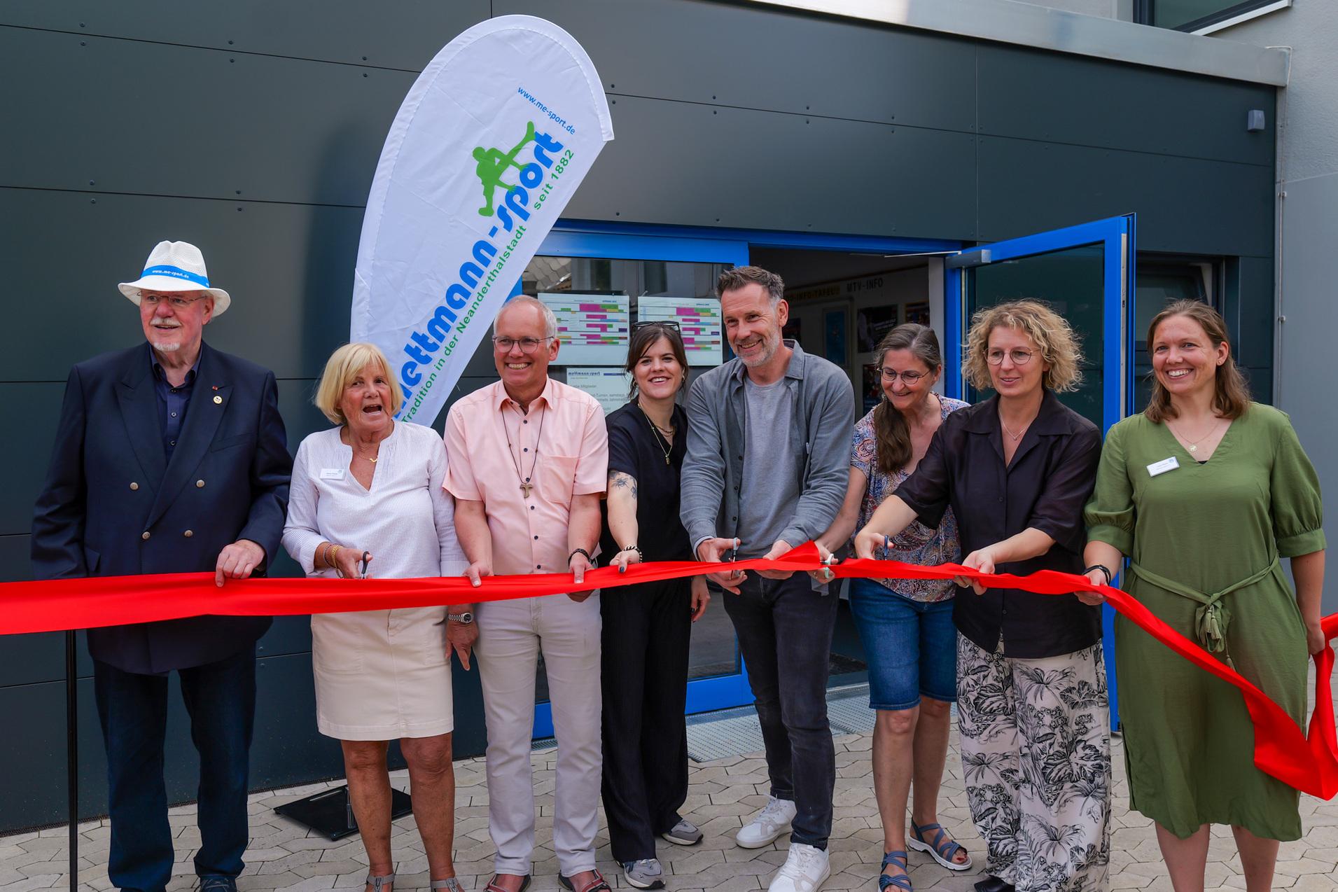 Eröffnungszeremonie mit mehreren Personen, die ein rotes Band vor einem neuen Gebäude durchschneiden.