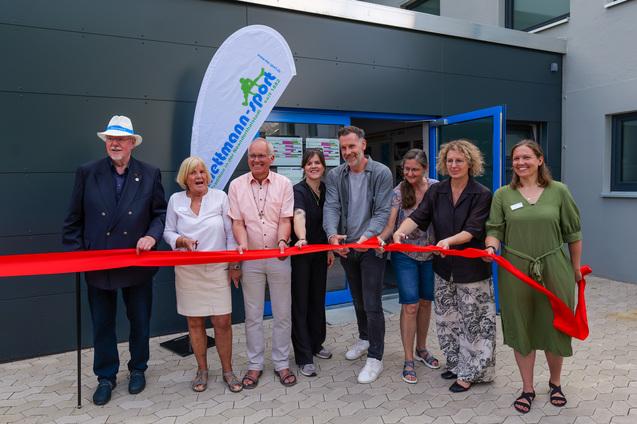 Eröffnungszeremonie mit mehreren Personen, die ein rotes Band vor einem neuen Gebäude durchschneiden.