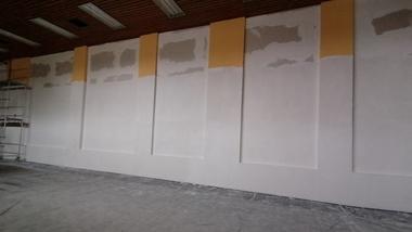 Unfertigte Wand mit Gelb- und Weißtönen sowie überlackierten Kanten in einem Raum mit Abdeckfolie auf dem Boden.