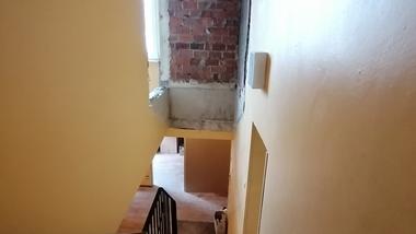 Blick die Treppe hinunter, im Hintergrund eine unvollendete Wand aus Ziegelsteinen und gelb gestrichene Wände.
