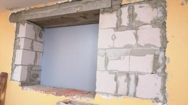 Öffnung in einer Wand mit Mauerwerk, umgeben von frischer Putzoberfläche, an einer gelben Wand.