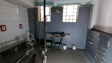 Baugleiches Zimmer mit grauen Wänden, Leitern, Werkzeugen und Fenster im Hintergrund.