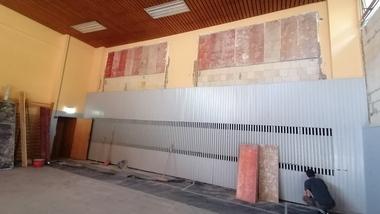 Leere Sporthalle mit unvollendeter Wandverkleidung, einem Arbeiter und Abdeckmaterial auf dem Boden.