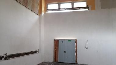 Leere Innenansicht eines Raumes mit einer grauen Tür und großen Fenstern an der Oberseite der Wand.