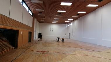 Leerer Raum mit Holzfußboden, hohen Wänden und Decke, Arbeitsutensilien und Kabeln sind sichtbar.