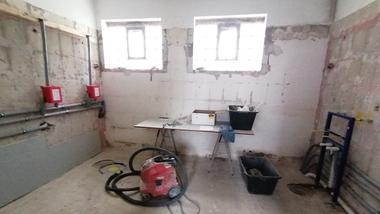 Blick in einen unvollendeten Raum mit vielen Baustellenmaterialien, einem Staubsauger und offenem Fenster.