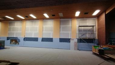 Innenansicht eines renovierungsbedürftigen Raums mit unvollendeten Wänden, Baugerüst und abgedecktem Boden.