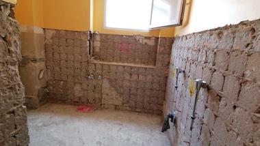 Renovierter Raum mit freiliegenden Wänden, sichtbaren Sanitäranschlüssen und einem geöffneten Fenster.