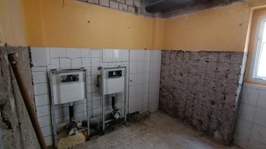 Rohbau eines Raums mit zwei Wandabläufen, unvollständiger Fliesenverkleidung und gelber Wandfarbe.